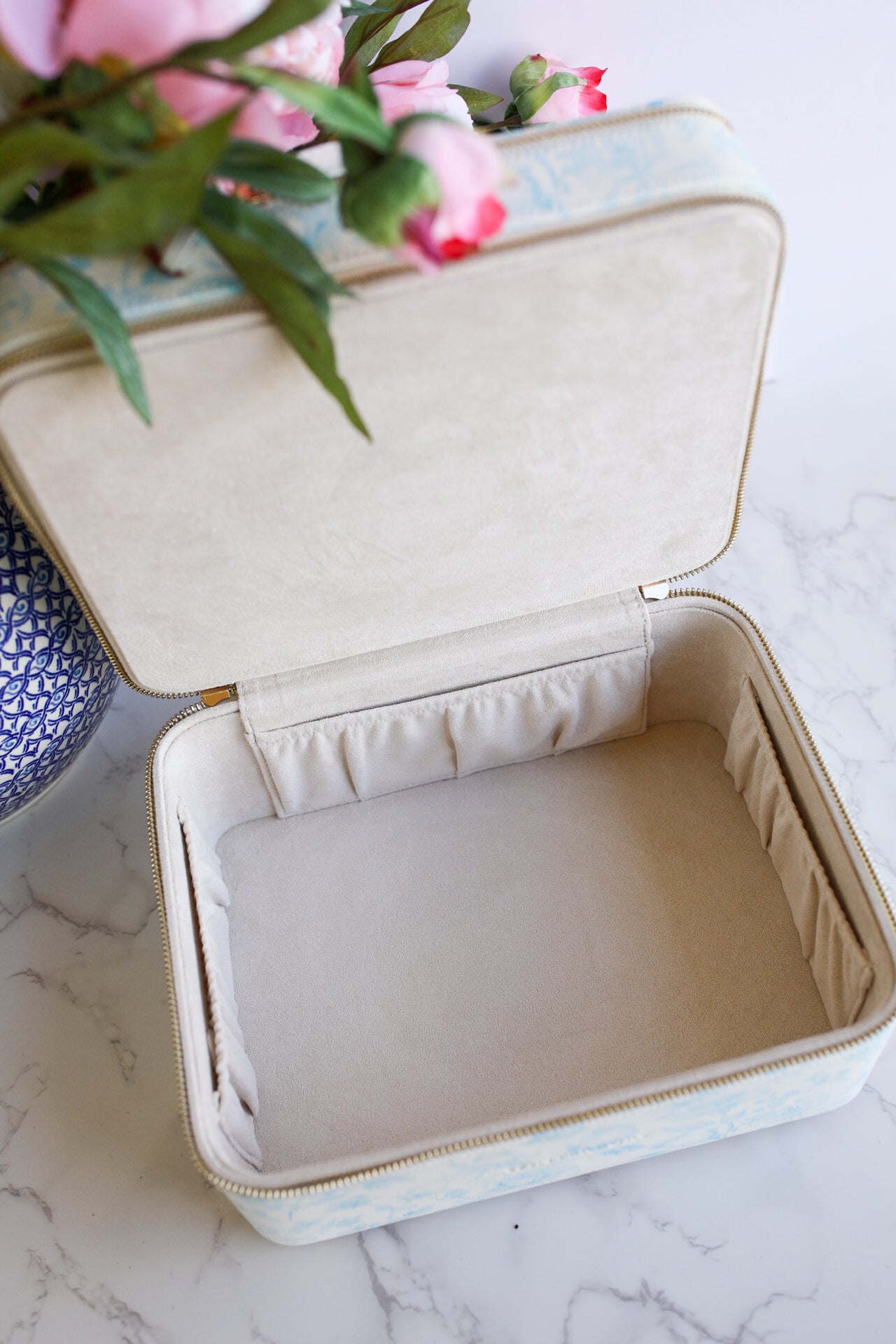 Beige jewelry case on a marble surface with flowers in the background