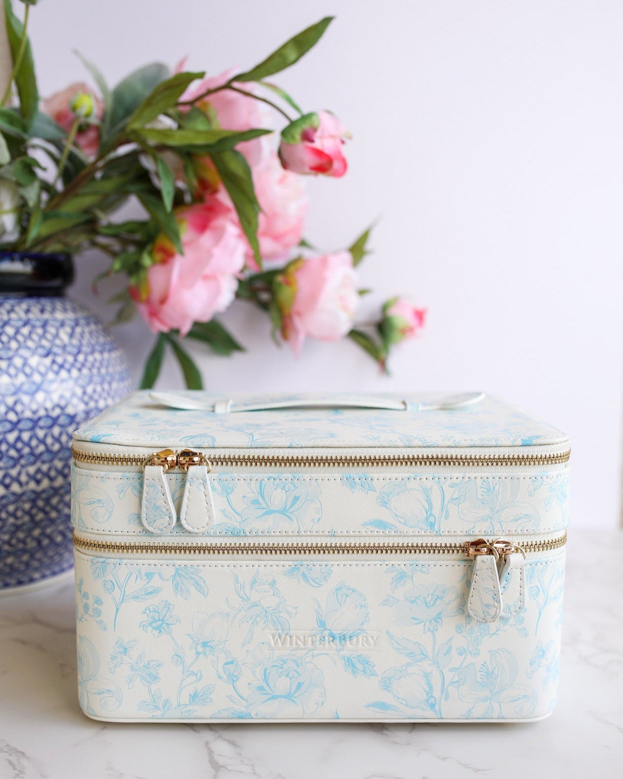 Floral-patterned travel case on a marble surface with pink flowers in the background