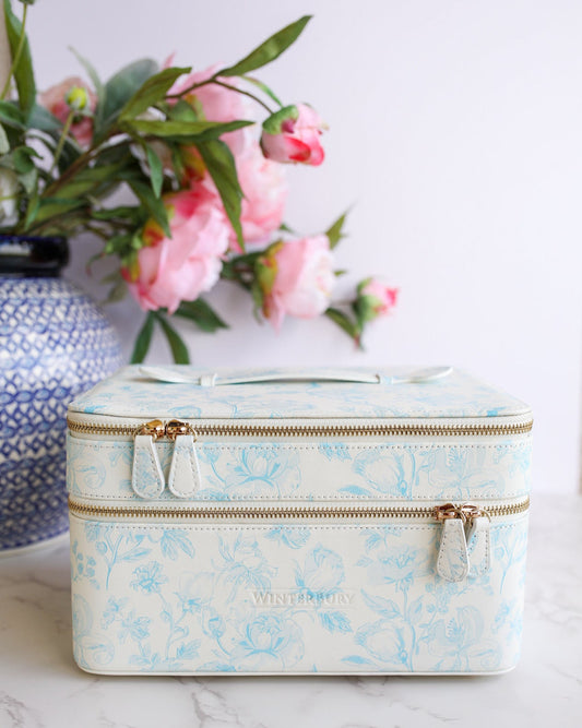 Floral-patterned travel case on a marble surface with pink flowers in the background